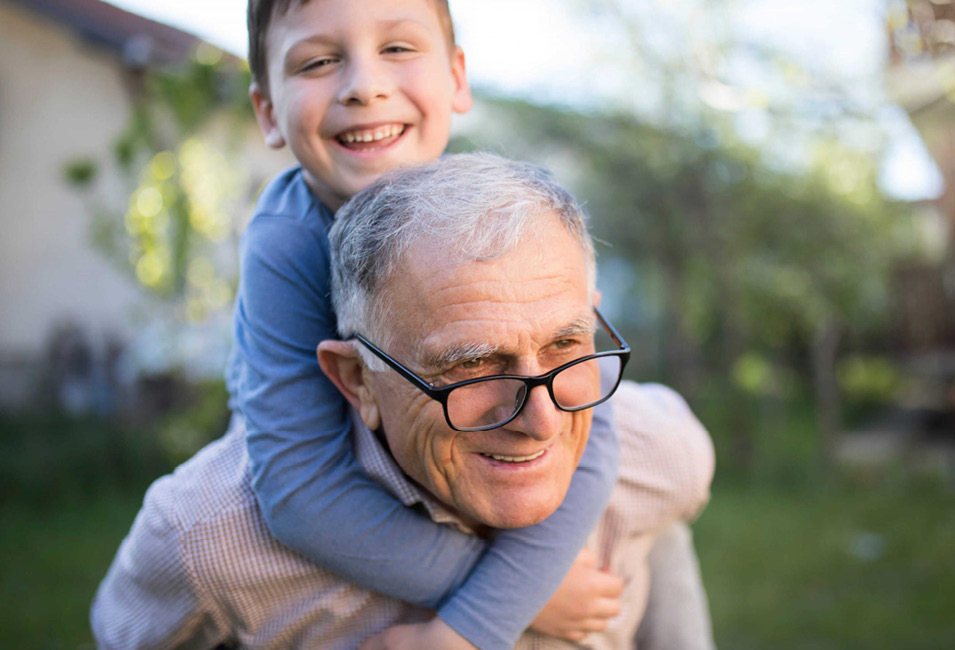 An older man carries his grandson on his shoulders.