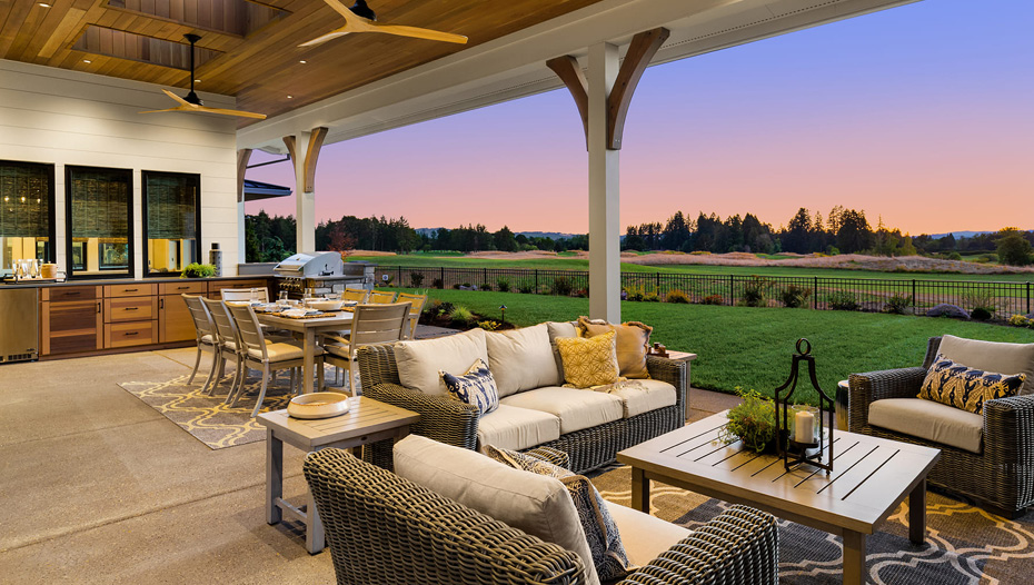 A large outdoor patio and yard with wicker furniture, grill, and dinner table.